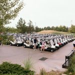 a photo between some trees of the golf carts lined up for the start of a charity golf tournament