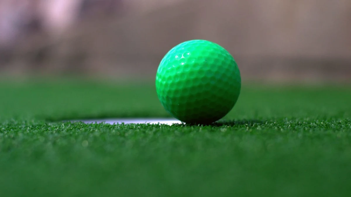 green golf ball on the green sitting by the cup