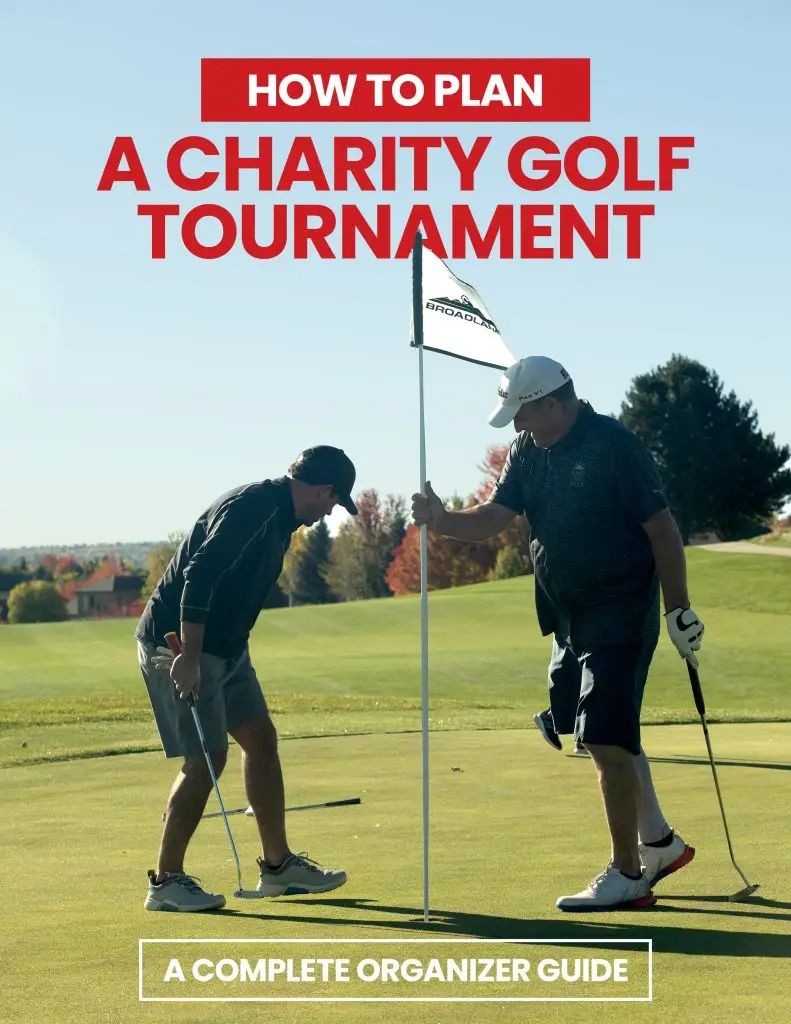 2 golfers on a putting green about to pull a pin flag up so that they can attempt a putt during a charity golf tournament
