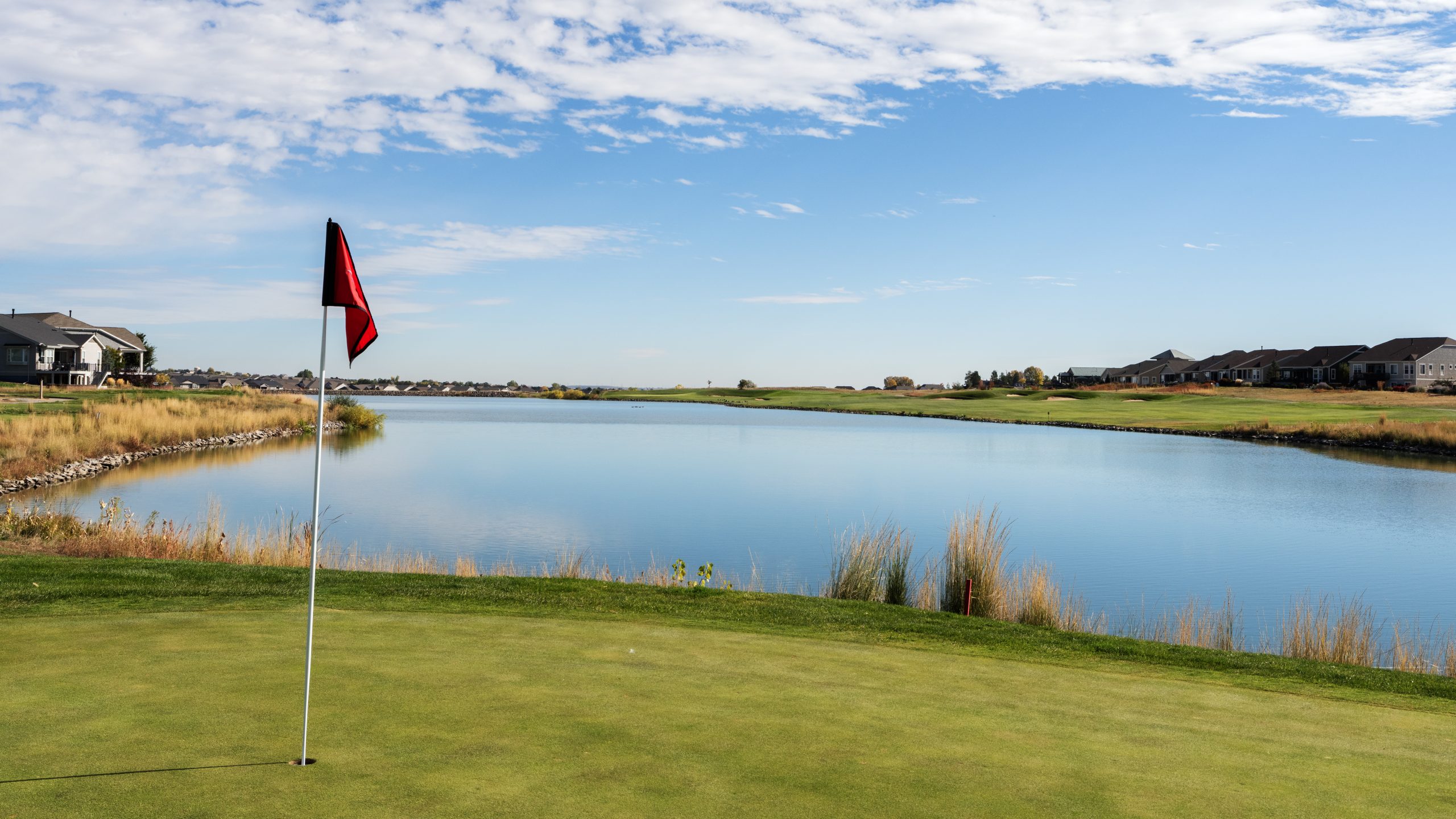 todd creek golf course on green with pin flag and water in the background