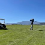 golfer swinging a club on the fairway with mountains in the background