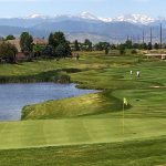 golf course green with pin flag, water to the left, and mountains in the background