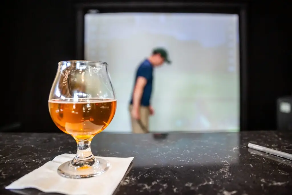 Beer on the bar in front of a golf simulator bay at The Birdie Bar in Louisville